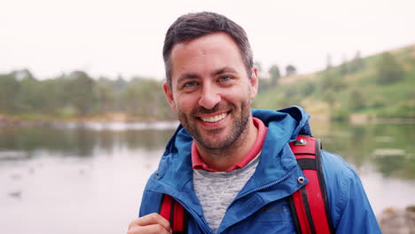 Adult-man-on-a-camping-holiday-standing-by-a-lake-smiling,-close-up,-Lake-District,-UK