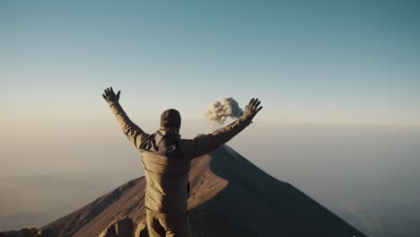 hiker on acatenango volcano raising arms at sunrise, looking at fuego volcano in antigua, guatemala