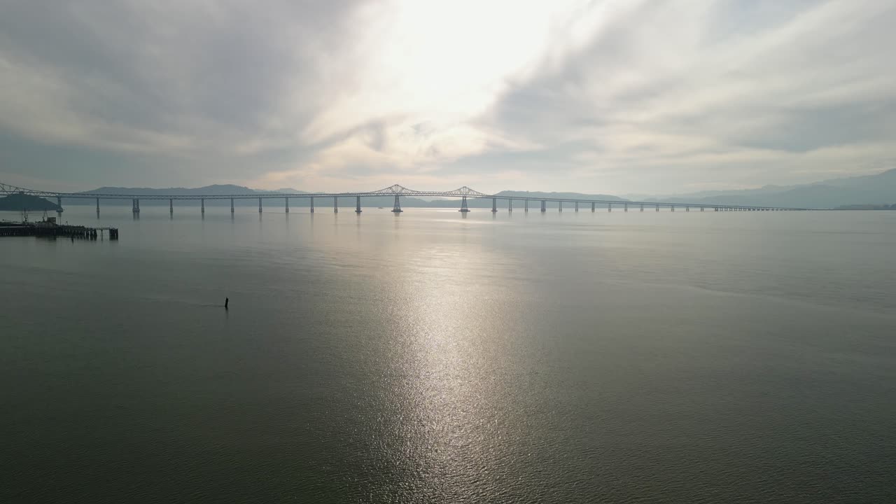 Ascending aerial drone shot that captures the Richmond–San Rafael Bridge stretching across the bay near Point Molate.