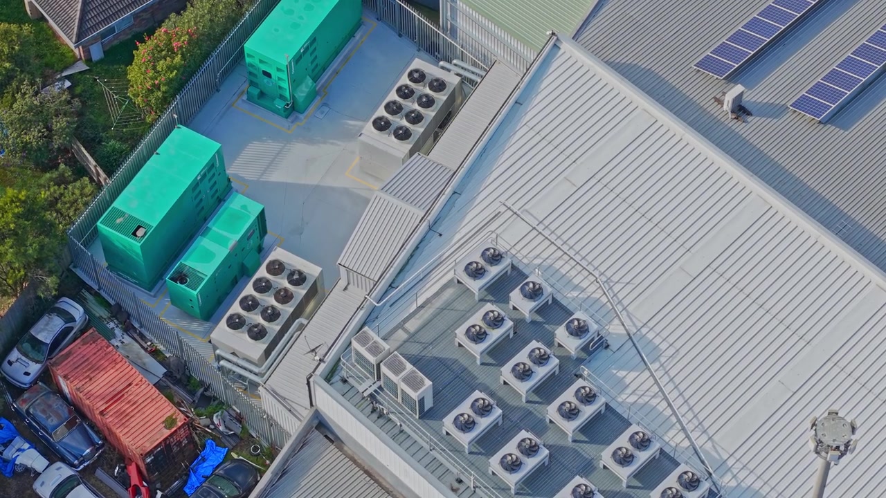 Crisp daylight drone video captures a rooftop filled with HVAC units, green generators, and solar panels. Industrial details, clean lines, and strong shadows highlight modern infrastructure.