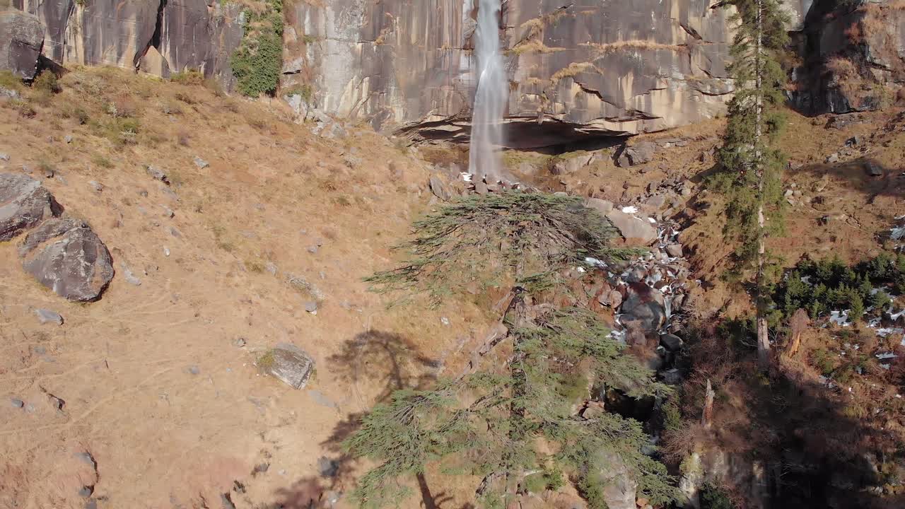 toma aérea de personas jugando debajo de las cascadas jogini cerca de manali, himachal pradesh durante el invierno, filmada con un dron volando sobre grandes árboles en 4k