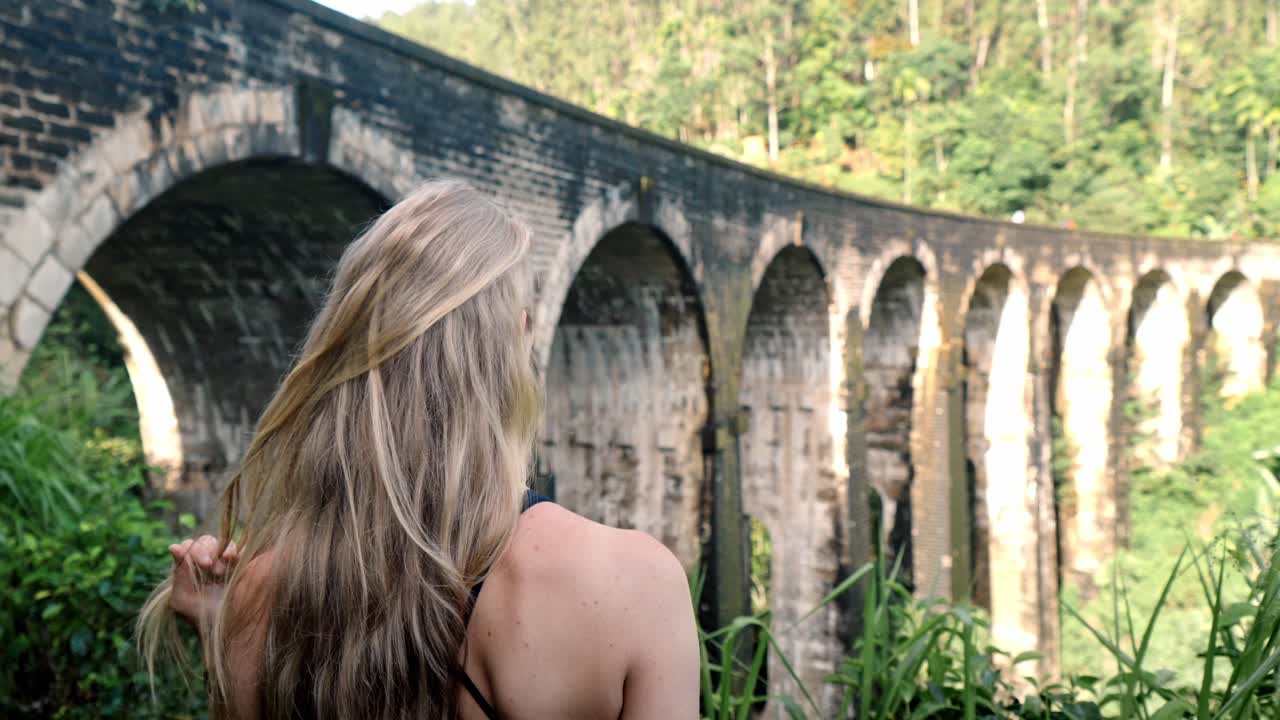 A young woman observes the historic Nine Arch Bridge from a nearby hillside in Ella, Sri Lanka.
