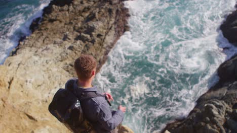 Un-Alto-ángulo-De-Vista-De-Un-Hombre-Mirando-Hacia-Abajo-Y-Arrojando-Rocas-Al-Océano-Desde-El-Borde-De-Un-Acantilado