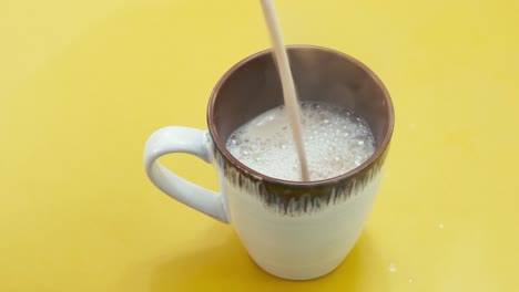 verter café cremoso caliente en la taza en la superficie amarilla