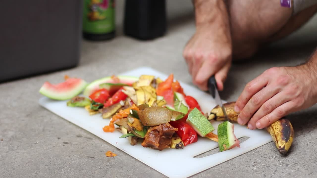 persona masculina cortando restos de comida a bordo para compost durante el día, primer plano
