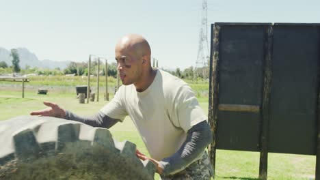 fit african american male soldier rolling tractor tyre on army obstacle course in the sun