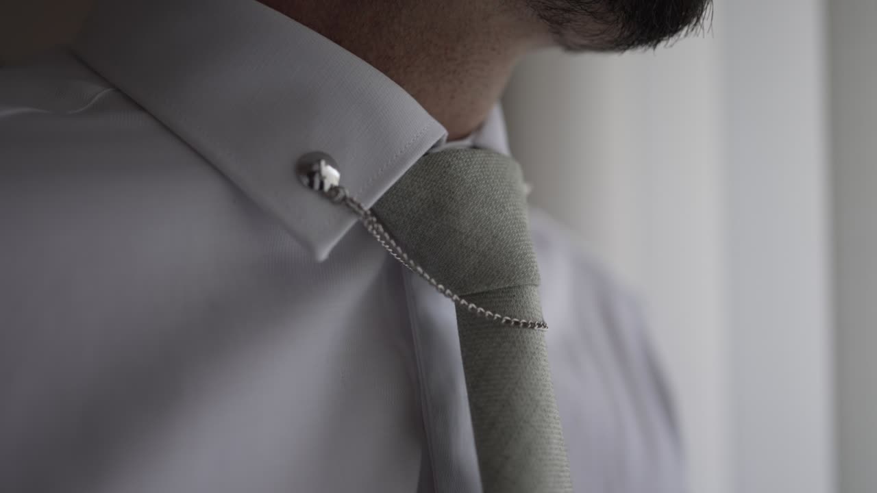 Close-up of a man's white dress shirt collar with a tie chain and grey tie