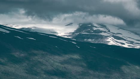 grey-white clouds flowing over the mountains casting shadows below