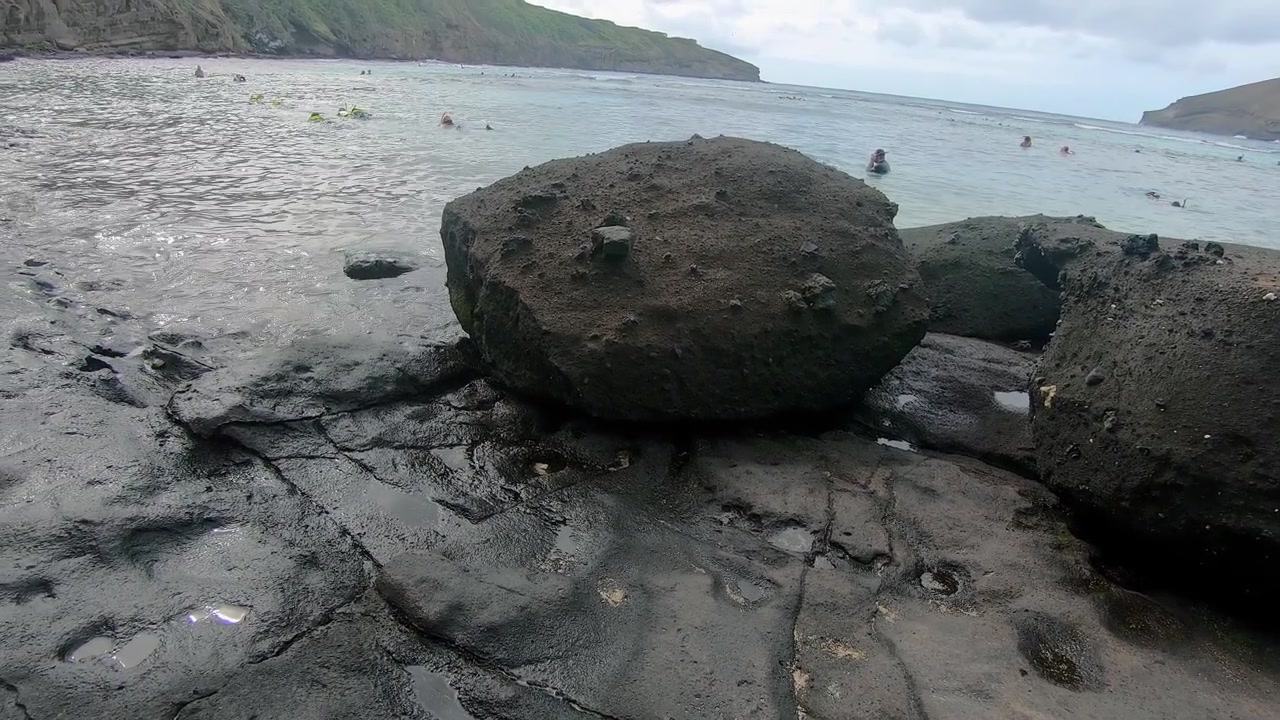 Rocce e lastre vulcaniche nella risacca sulla spiaggia dell'Hanauma Bay State Park e Riserva Naturale sull'isola di Oahu, Hawaii.