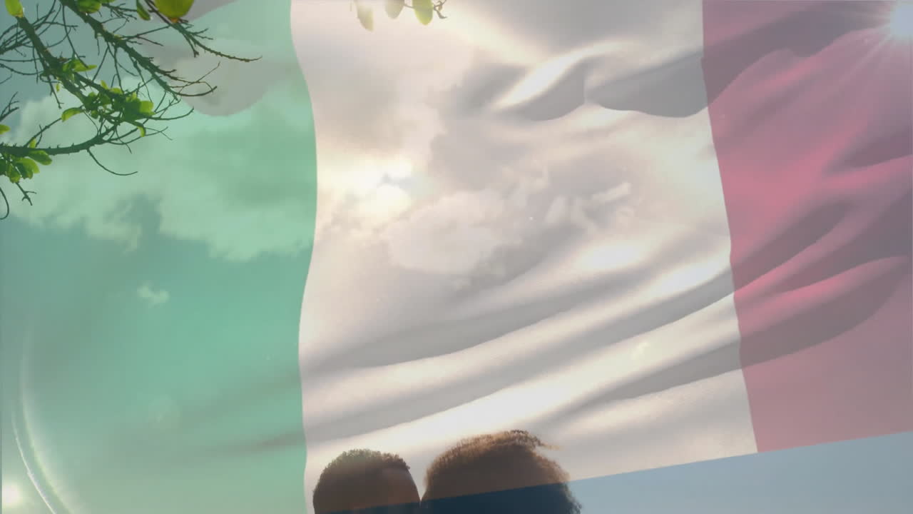 Coppia che si abbraccia sotto un cielo soleggiato, tenendo insieme una bandiera italiana sventolante.