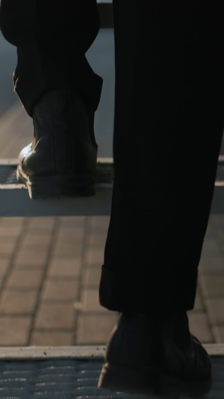 Back leg view man black shoe and trouser climbing staircase carefully with warm soft light reflecting off interlocked stone path, slow deliberate step, focus on movement