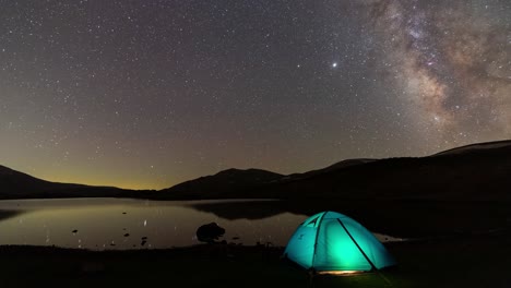 blue tent camping near the calm relax lake like a mirror lantern light inside the camping and milky way nebula move in starry night sky