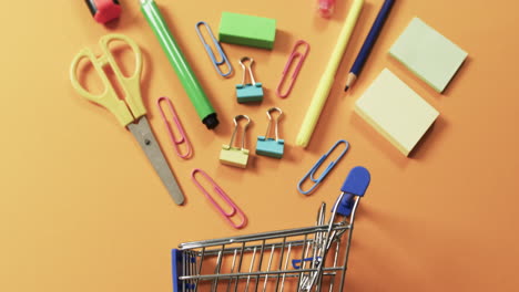 vista aérea del carrito de compras y los artículos escolares sobre un fondo naranja
