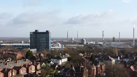 Aerial-view-over-park-trees-to-St-Helens-industrial-townscape-with-blue-skyscraper,-Merseyside,-England