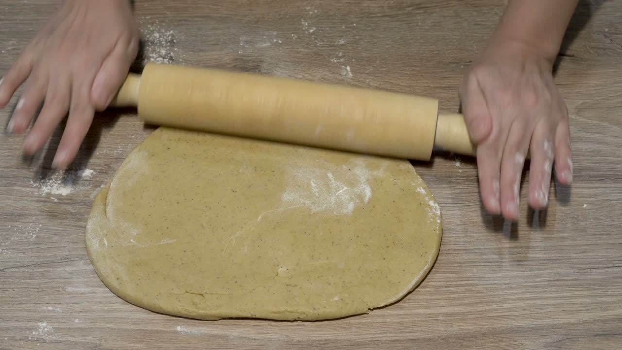 una mujer enrolla masa cruda amarilla en un panqueque delgado con un rodillo de madera en una cocina de casa. primer plano. vista superior. 4k.