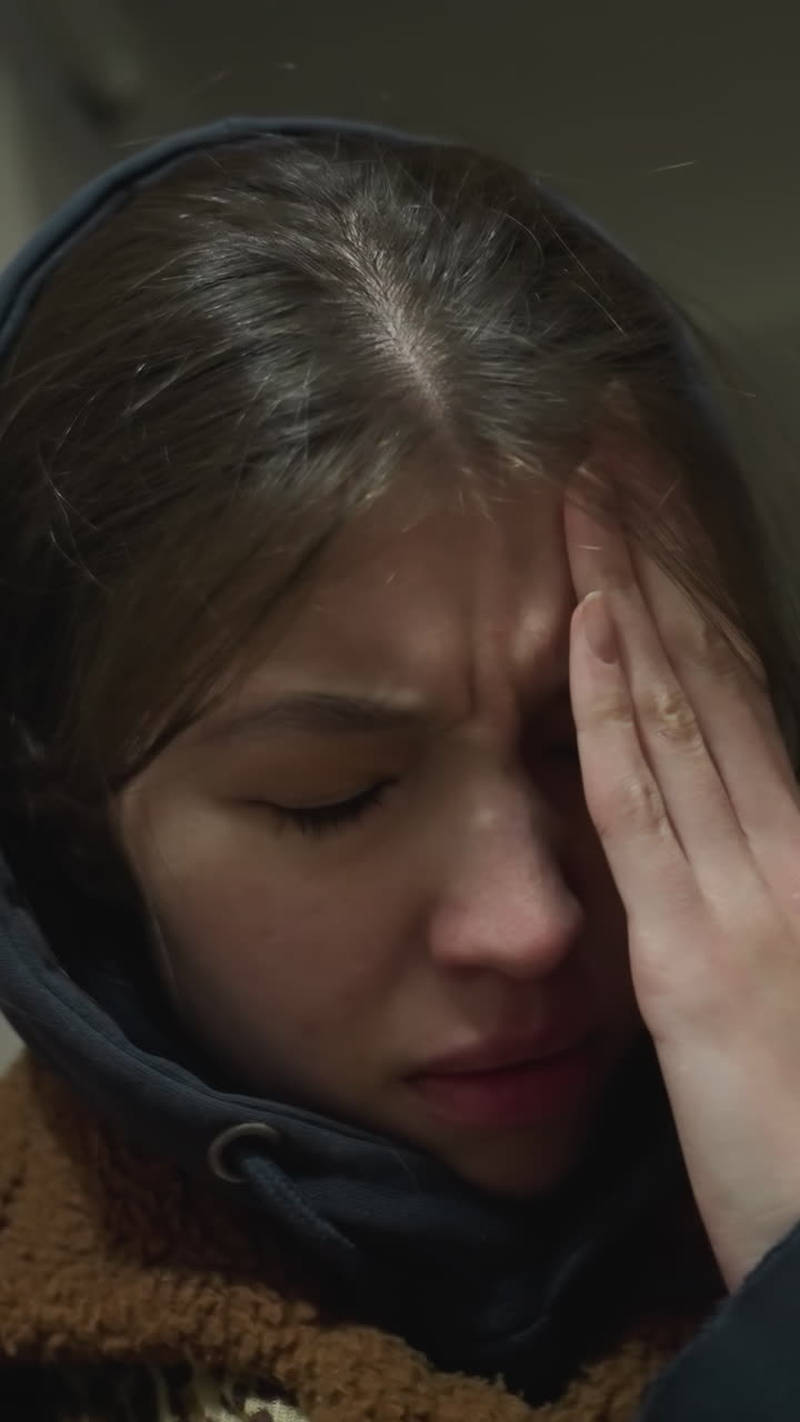 un primer plano de una chica triste con un abrigo marrón apoyada en la pared de un túnel subterráneo. ella está sosteniendo su cara con una mano, sus ojos cerrados, transmitiendo una profunda tristeza y dolor emocional