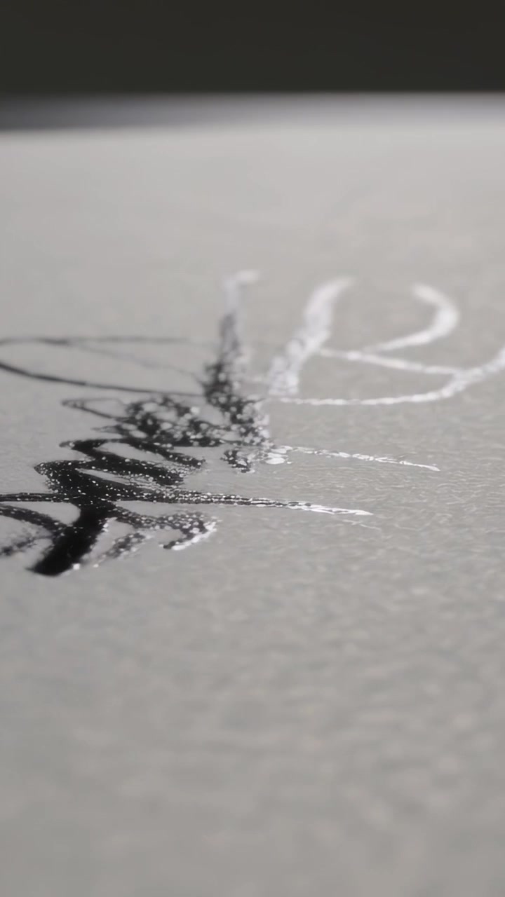 Vertical video: Appearing fingers nearing wet black ink loops on rough paper at desk checking gloss