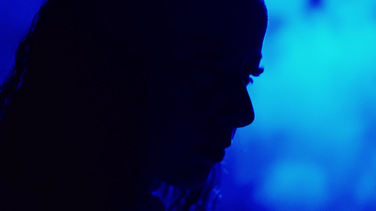 Profilo cinematografico scuro di una donna illuminata da una luce blu intensa: concept visivo misterioso e suggestivo
