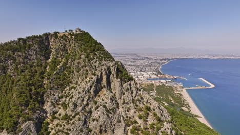 Antalya-Turquía-Aérea-V51-Dramático-Paso-Elevado-De-Drones-Ladera-Rocosa-De-La-Cumbre-De-La-Montaña-Tünek-Tepe-Capturando-La-Costa-De-La-Playa-Y-El-Paisaje-Urbano-De-Liman-Konyaaltı-En-Verano---Filmado-Con-Mavic-3-Cine---Julio-De-2022