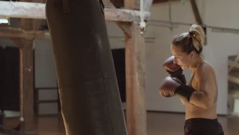 medium shot of tired female boxer training with punching bag