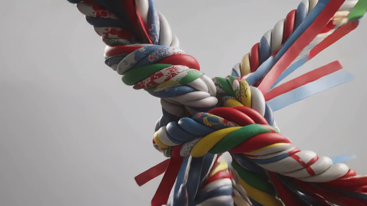 Falling patterned ribbon cords twisting toward center in studio, forming tightening knot with tails