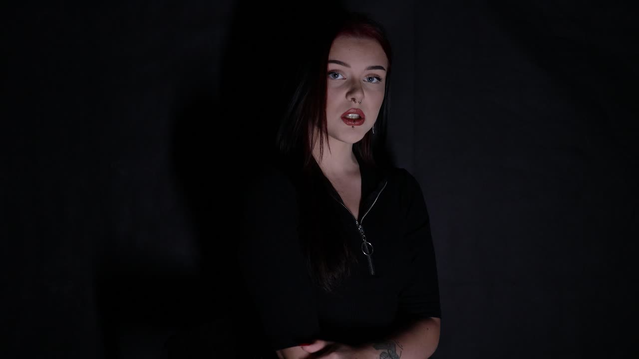 atractiva joven mujer caucásica cantando frente a un fondo negro mientras está iluminada con luz blanca