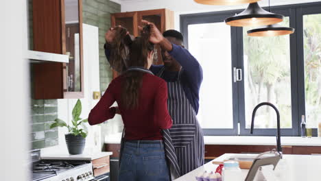 Feliz-Pareja-Diversa-Usando-Delantales-En-La-Cocina-Y-Usando-Tableta,-Cámara-Lenta