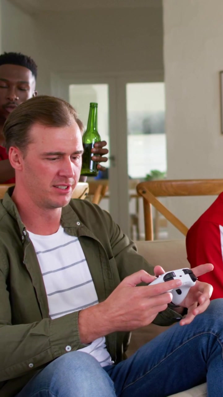 Vertical video: Removing VR headset, man in red sports shirt on couch at home, letting friend play
