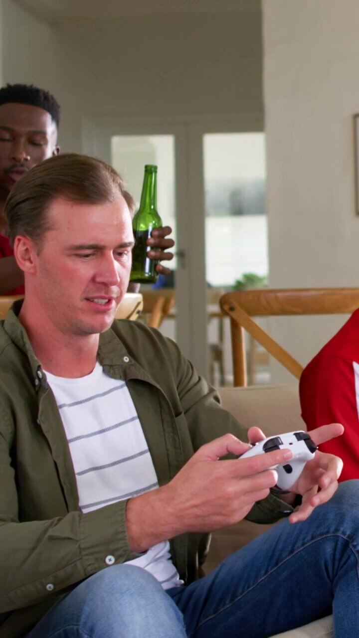 Vertical video: Removing VR headset, man in red sports shirt on couch at home, letting friend play