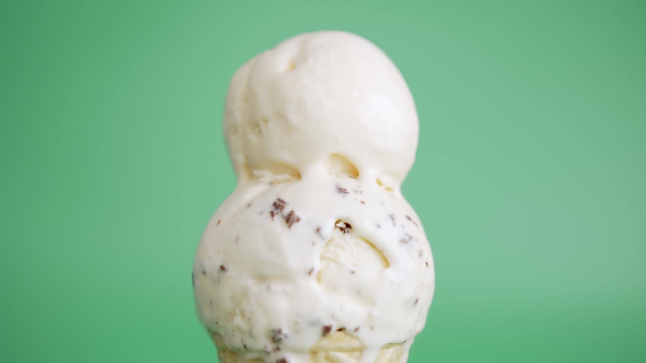 Mani che prelevano gelato alla vaniglia con gocce di cioccolato in un cono waffle.