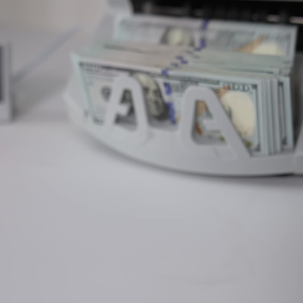 Macchina conta soldi bianca sul tavolo bianco. Mazzo di dollari americani contato nell'apparecchiatura. Una mano prende una risma di banconote mostrandole più vicino alla fotocamera.