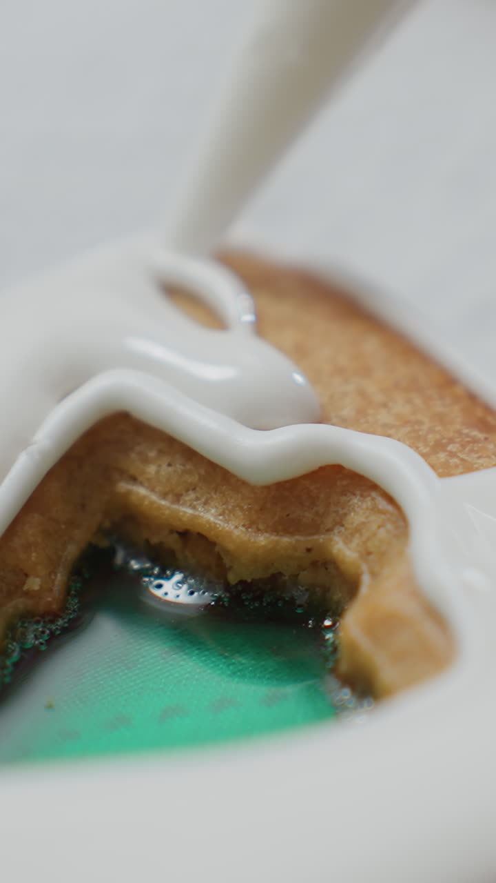 초록색 채우기와 함께 텍스처 된 종이에 놓인 쿠키에 대한 섬세한 아이싱 프로세스의 클로즈업, 색 아이싱이 복잡한 장식을 위해 녹색 액체를 조심스럽게 고 있습니다.