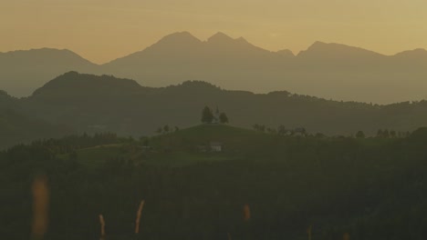A serene hillside with distant mountains at sunset creates a peaceful landscape scene