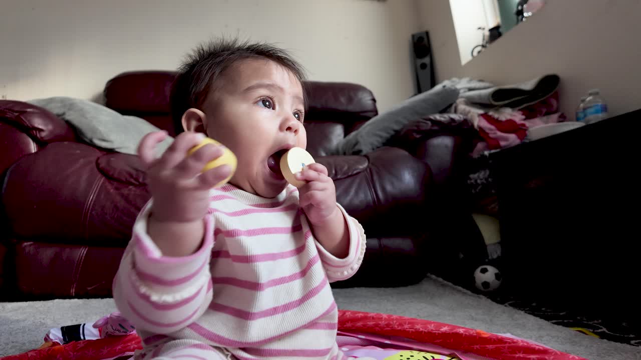 Cute baby chewing on a wooden toy while sitting on a playmat indoors
