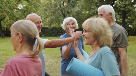 sporty senior people greeting female fitness coach and friends in park