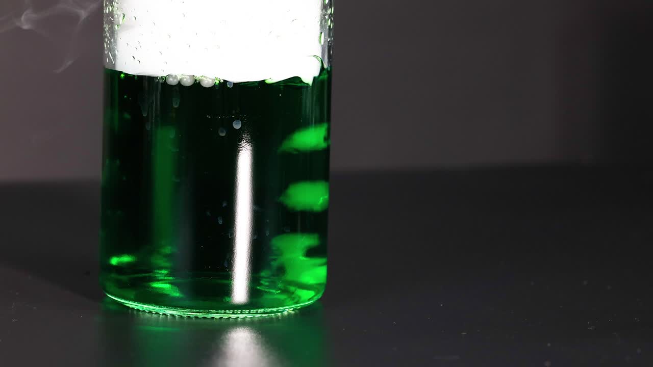 un vaso con líquido verde reacciona con hielo seco, creando burbujas y vapor en un entorno controlado