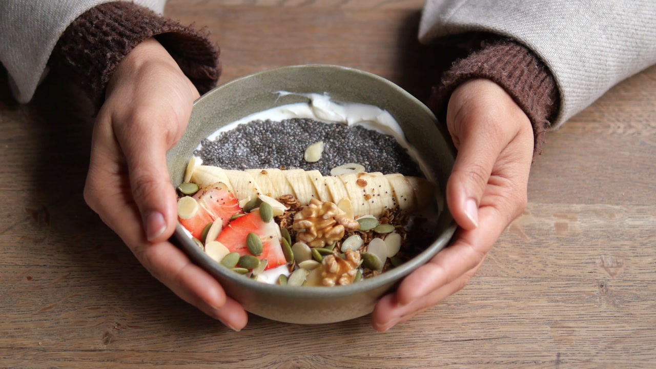 Hands Holding a Healthy Breakfast Bowl with Yogurt, Fruit, and Nuts