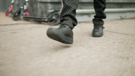 leg view of person in patterned pants and black shoes stepping down concrete stairs outside school building, blurred scooter parked nearby