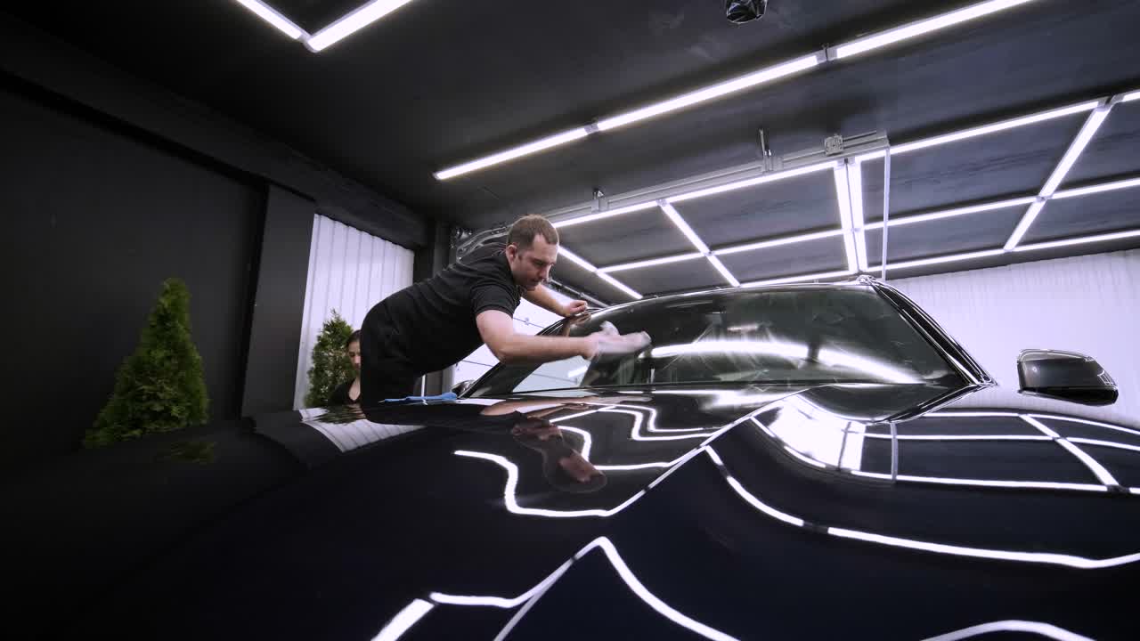 el lavador de coches profesional con guantes negros limpia el coche después de lavar y forrar la cerámica. conceptos de: trabajo profesional, varias herramientas de lavado, limpieza para brillar.