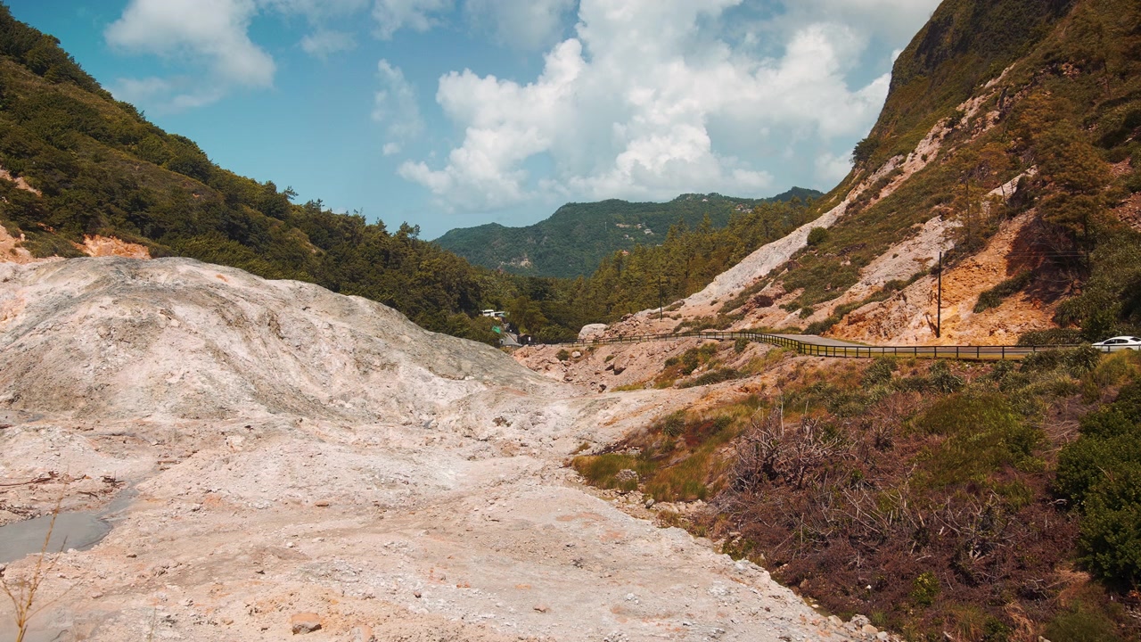 Vista panoramica del vulcano Soufrière Drive-In a Saint Lucia, che mostra formazioni rocciose solforose pallide, montagne verdi lussureggianti e il sentiero tortuoso attraverso il paesaggio geotermico