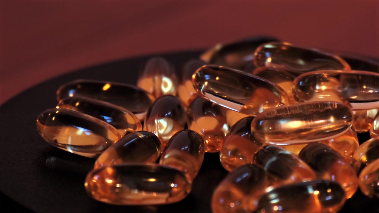 Illuminazione calda su capsule softgel dorate su una superficie scura.