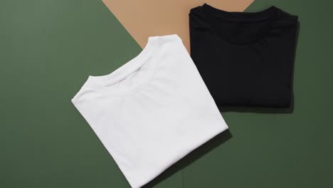 Video-of-flat-lay-of-folded-white-and-black-t-shirts-with-copy-space-on-green-and-brown-background