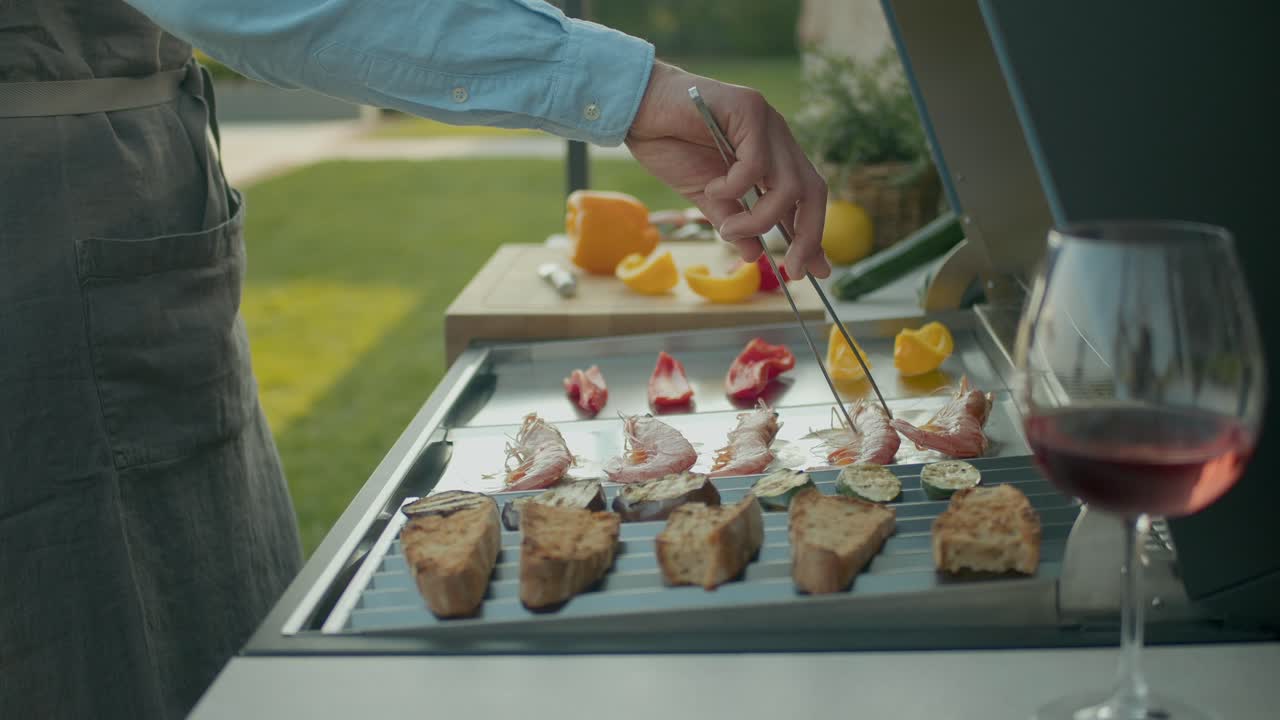 Close Up Shot Of Man Cooking Shrimps On Grill, With His Glass Of Wine Beside