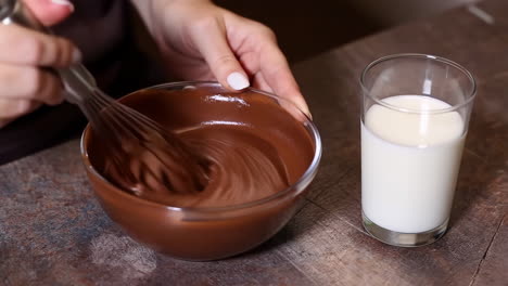 Person whisking melted chocolate in a bowl next to a glass of milk