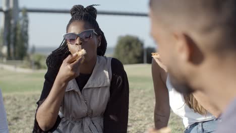 relaxed young people eating pizza in park.