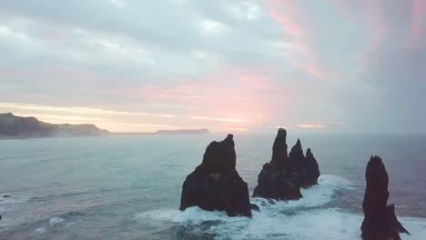 reynisdrangar rocks at reynisfjara beach next to vik i myrdal at south iceland. aerial drone shot flying over a cliff during sunrise. large storm waves crash rock. high resolution footage. 4k