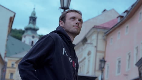 Young-man-wearing-all-black-looking-around-in-historical-European-town-Banska-Stiavnica-in-Slovakia-during-a-blue-hour-at-dusk