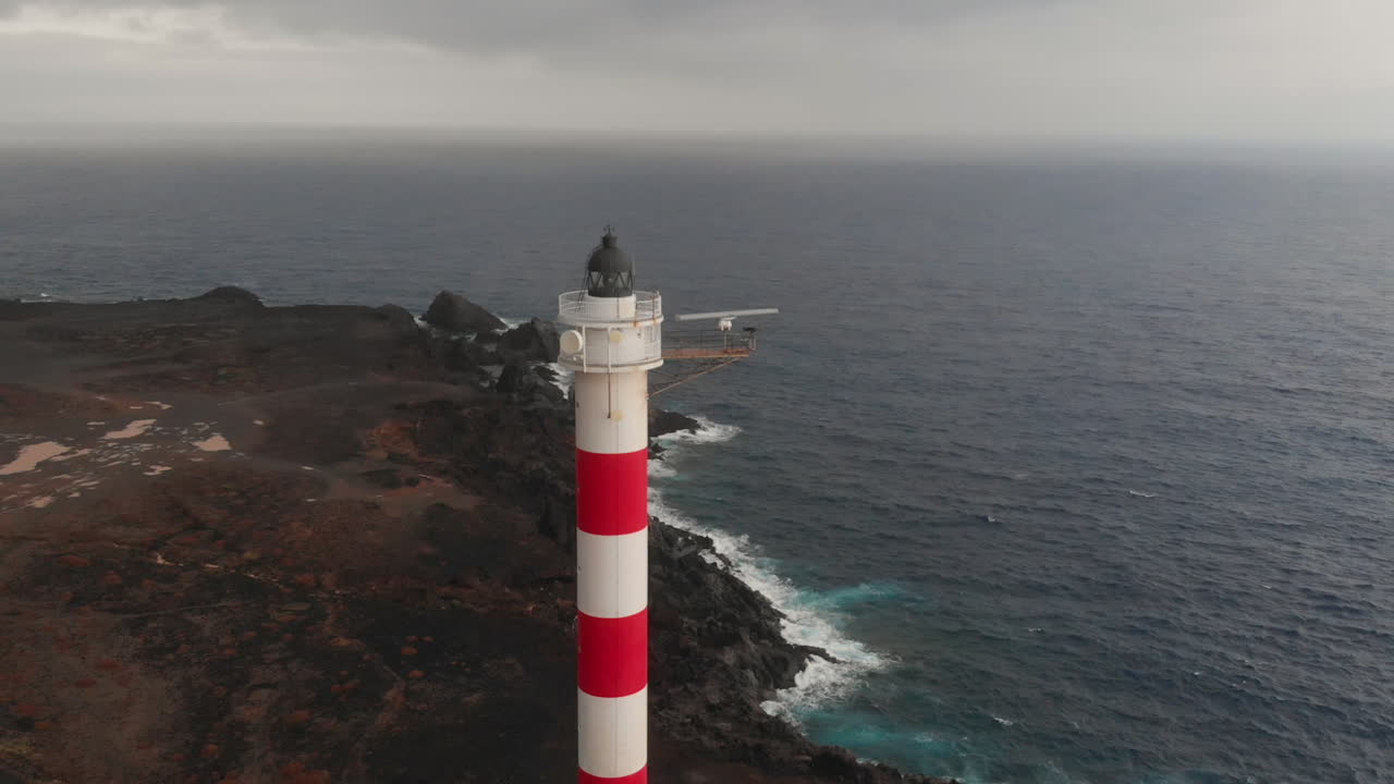 Close Aerial view rotating from right to left around red and white coastal lighthouse of Punta Rasca, Tenerife.
