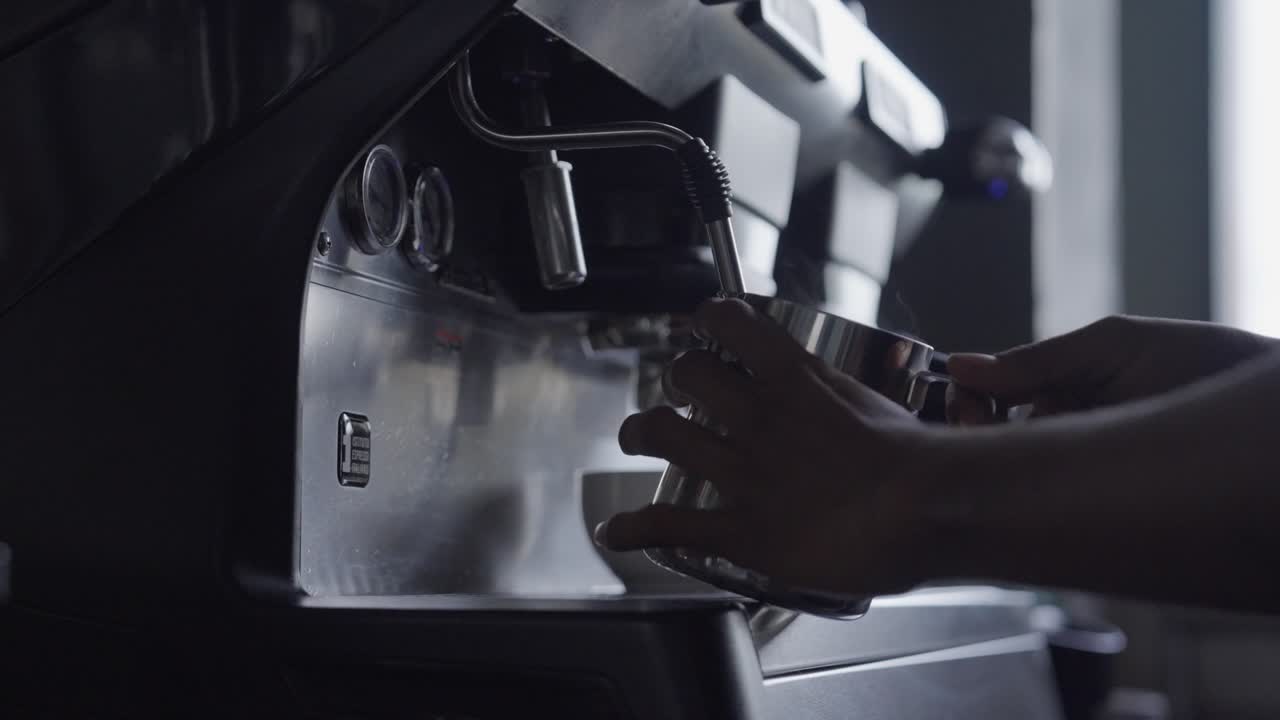 A steady high speed side close-up shot of coffee being poured from a coffee machine by a barista at a coffee shop