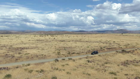 drone shot around a car driving across endless wasteland wilderness, sunny day